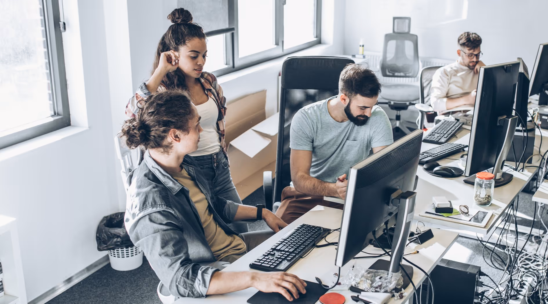 Vier junge Erwachsene arbeiten an Computern in einem hellen Büro.