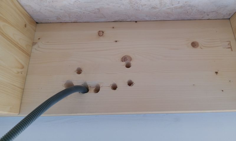 Panneau de bois percé de plusieurs trous et dans lequel est inséré un tuyau flexible gris.