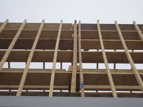Gros plan sur des poutres et des planches de bois formant une partie de la charpente du toit d'un bâtiment, sur fond de ciel gris.