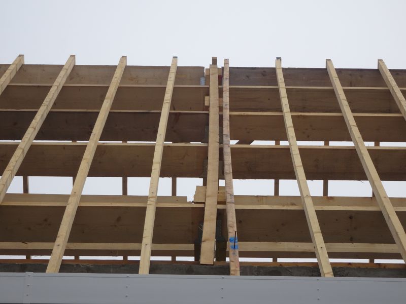 Gros plan sur des poutres et des planches de bois formant une partie de la charpente du toit d'un bâtiment, sur fond de ciel gris.
