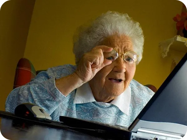 Elderly woman adjusting her glasses while looking at a laptop screen.