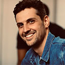 Jeune homme souriant avec une chemise en jean bleue, regardant vers la droite.