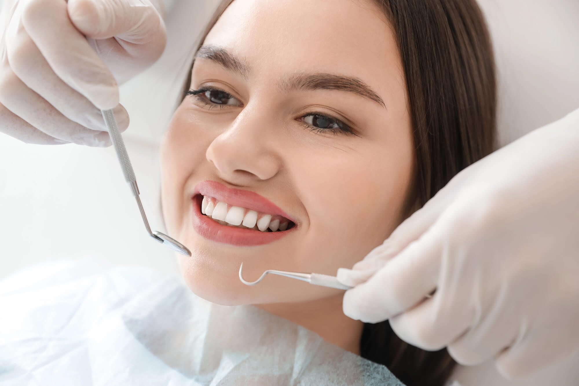 A close-up of a dental professional's hands, wearing gloves, using tools during a dental procedure on a patient.
