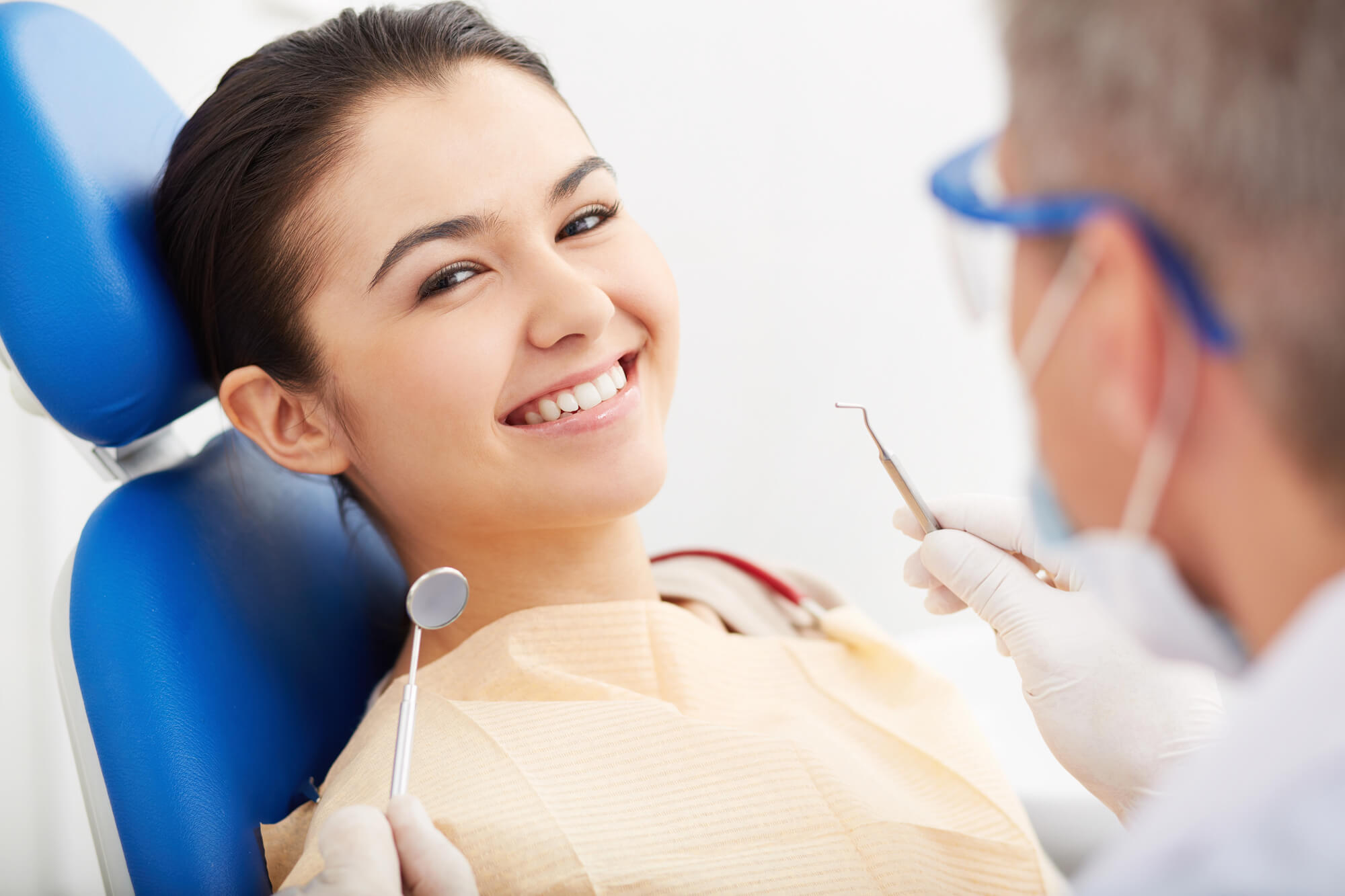 A dentist in gloves holds a dental tool while attending to a patient seated in a dental chair, wearing a protective bib.
