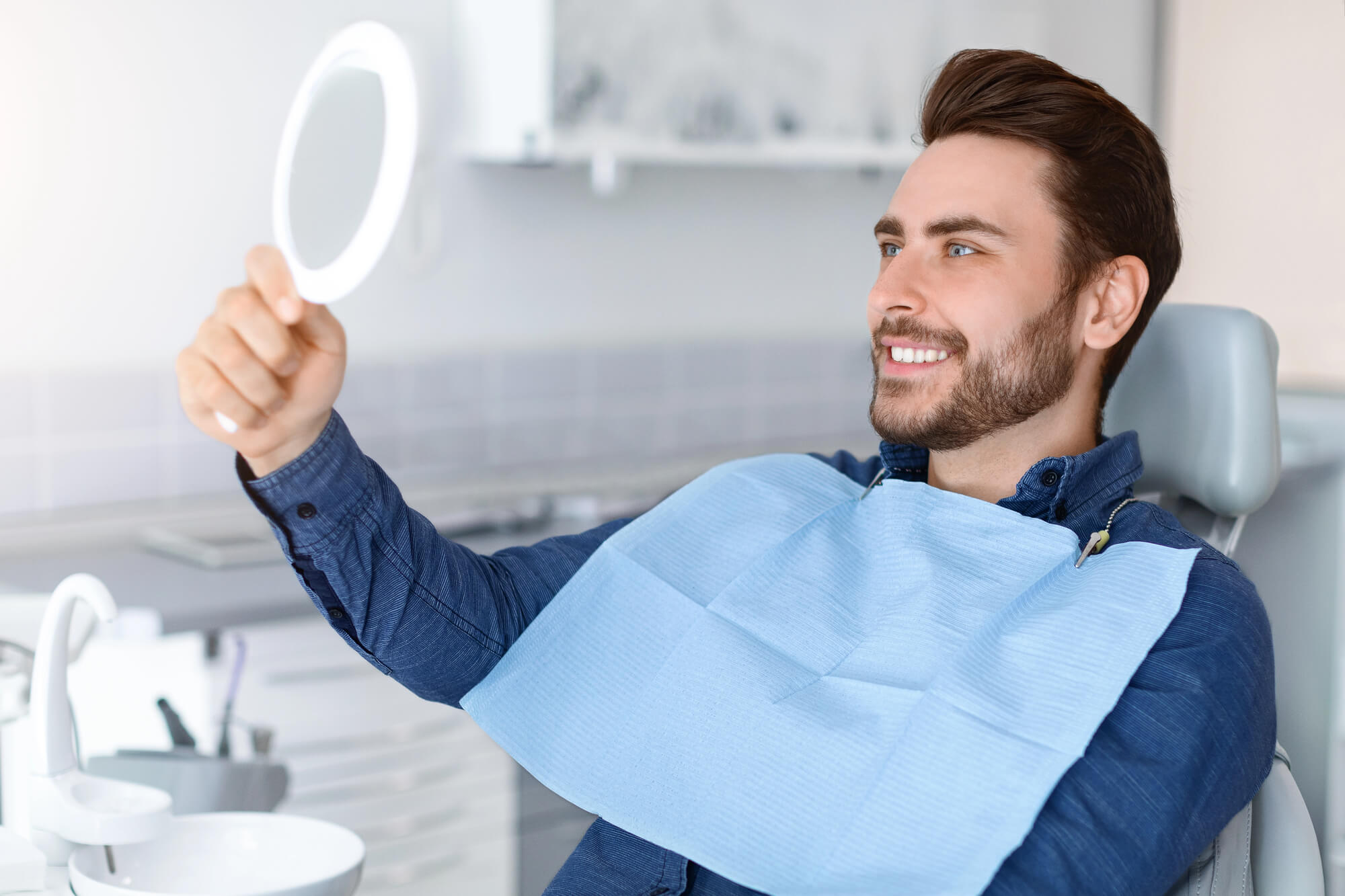 A man in a dental chair looking at himself in a handheld mirror