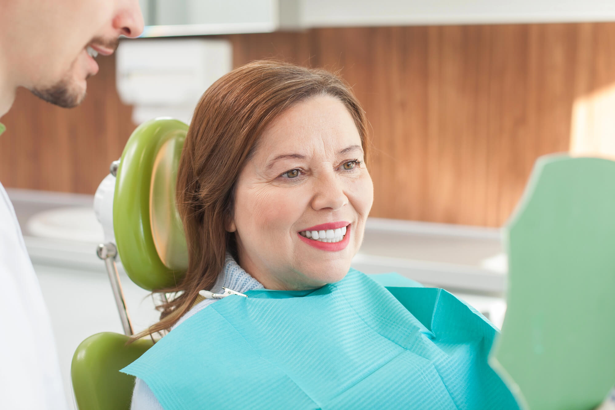 A woman in a dental chair looking at herself in a green mirror