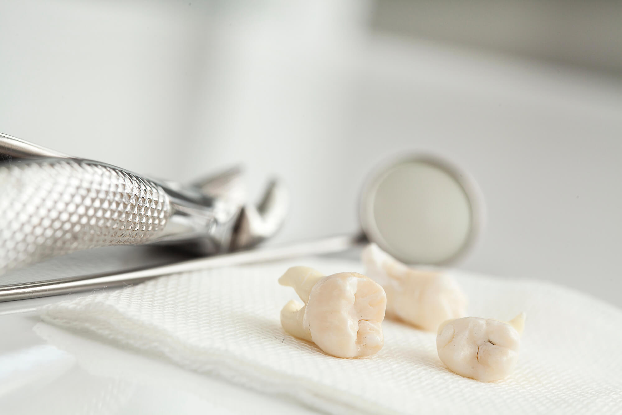 Extracted teeth on a hygienic surface beside dental tools, with a mirror reflecting a blurred clinical environment in the background.