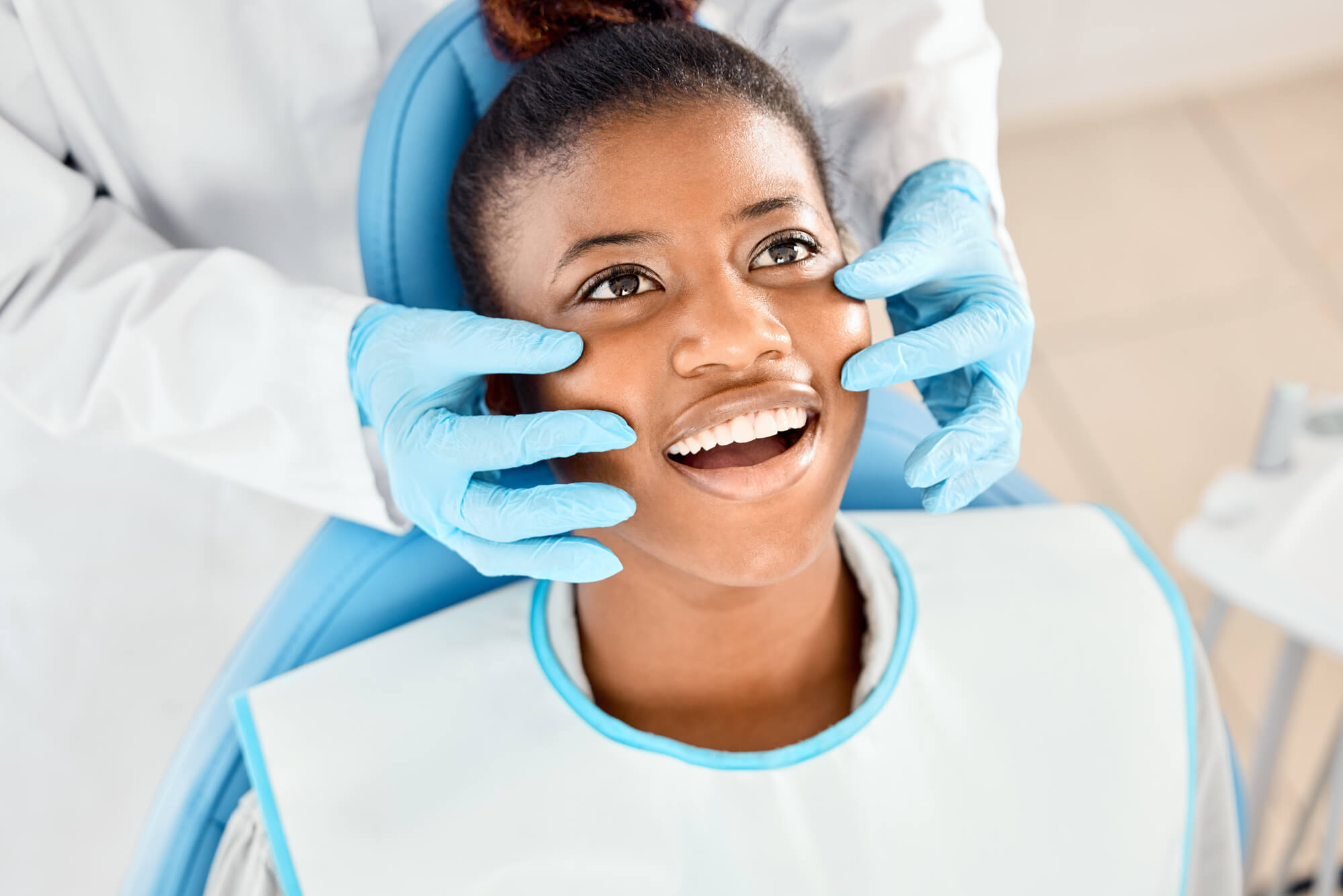 A dental professional in gloves prepares a patient for a procedure, featuring a dental chair and protective bib.