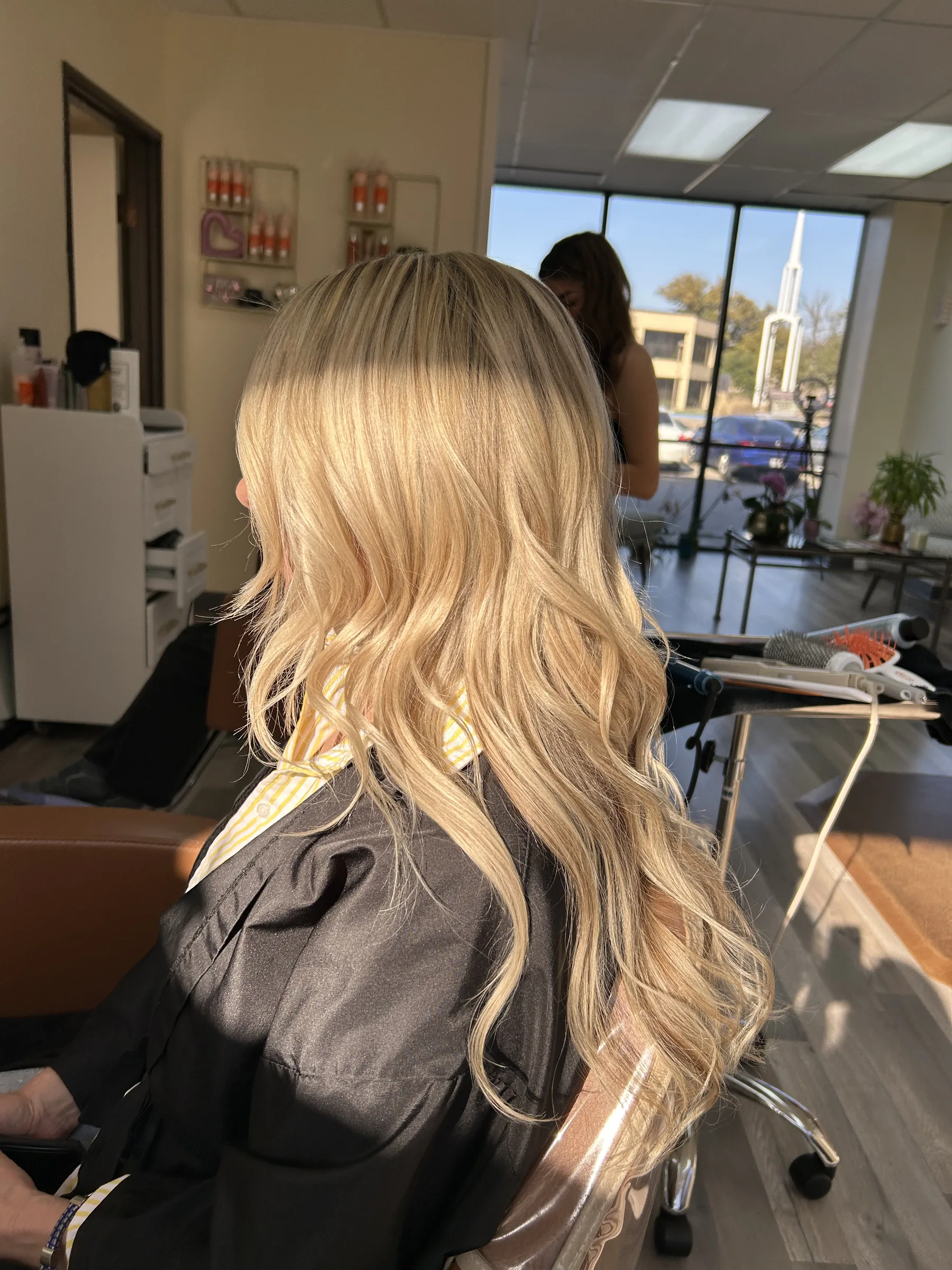 Side view of a person with long, wavy blonde hair sitting in a salon chair.