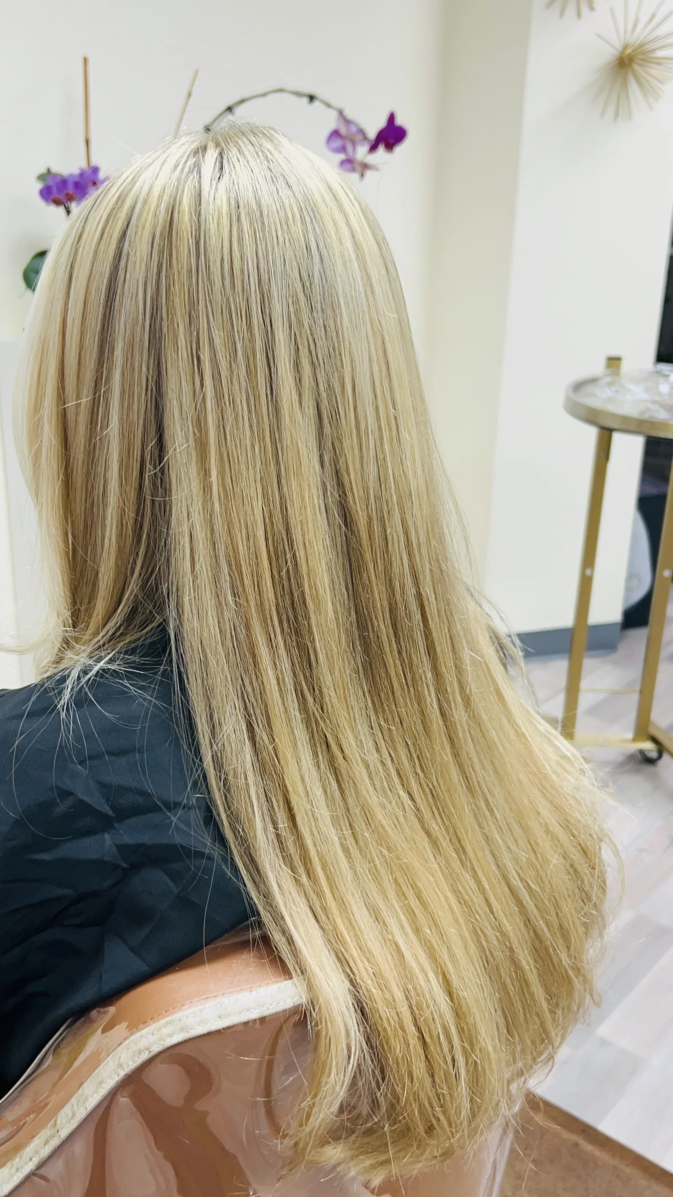 Back view of long, straight blonde hair on a person seated in a salon chair.