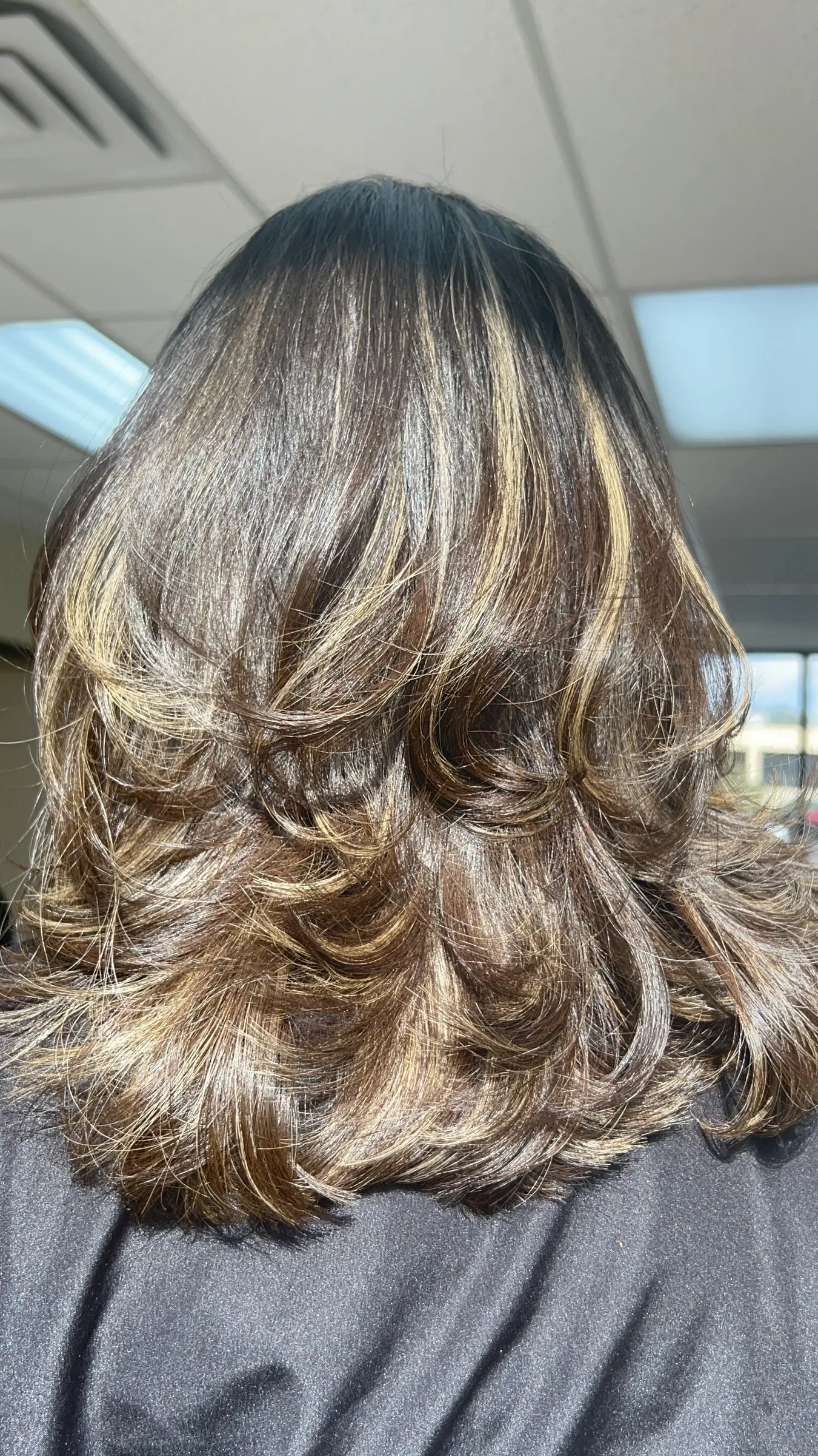 Back view of shoulder-length brown hair with blonde highlights and soft curls.