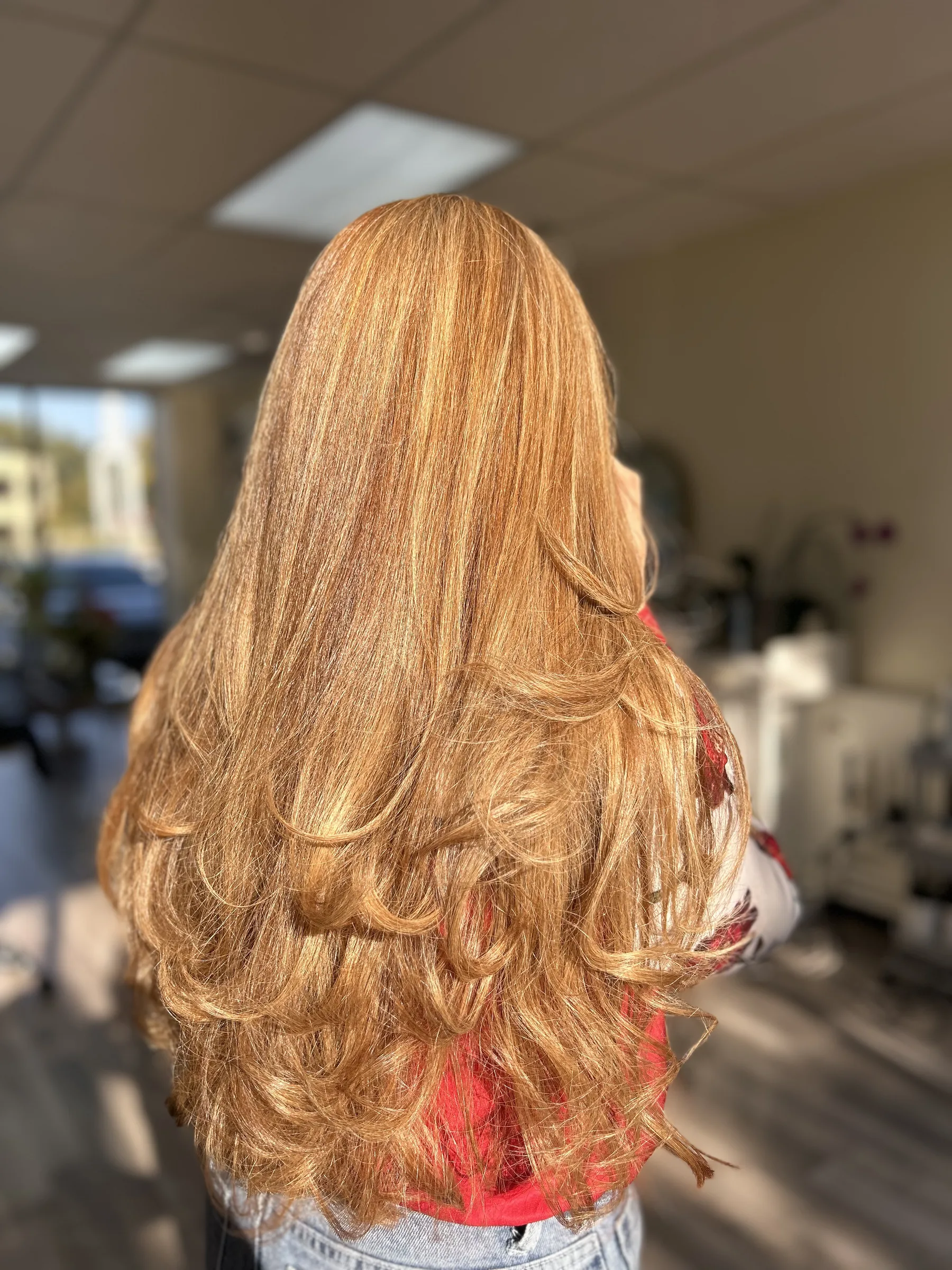 Person with long, voluminous golden blonde hair styled in soft curls standing indoors.