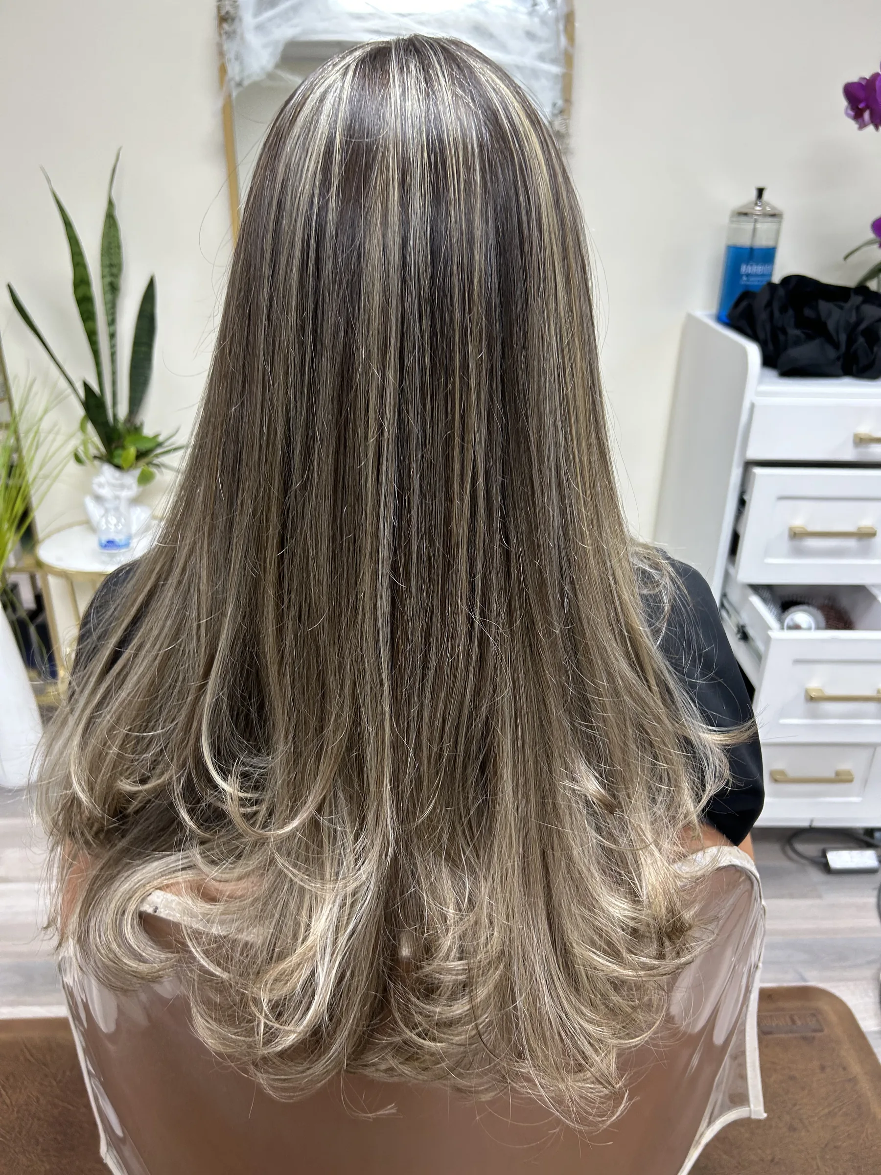 Back view of a person with long, straight, light brown hair with blonde highlights styled with curled ends.