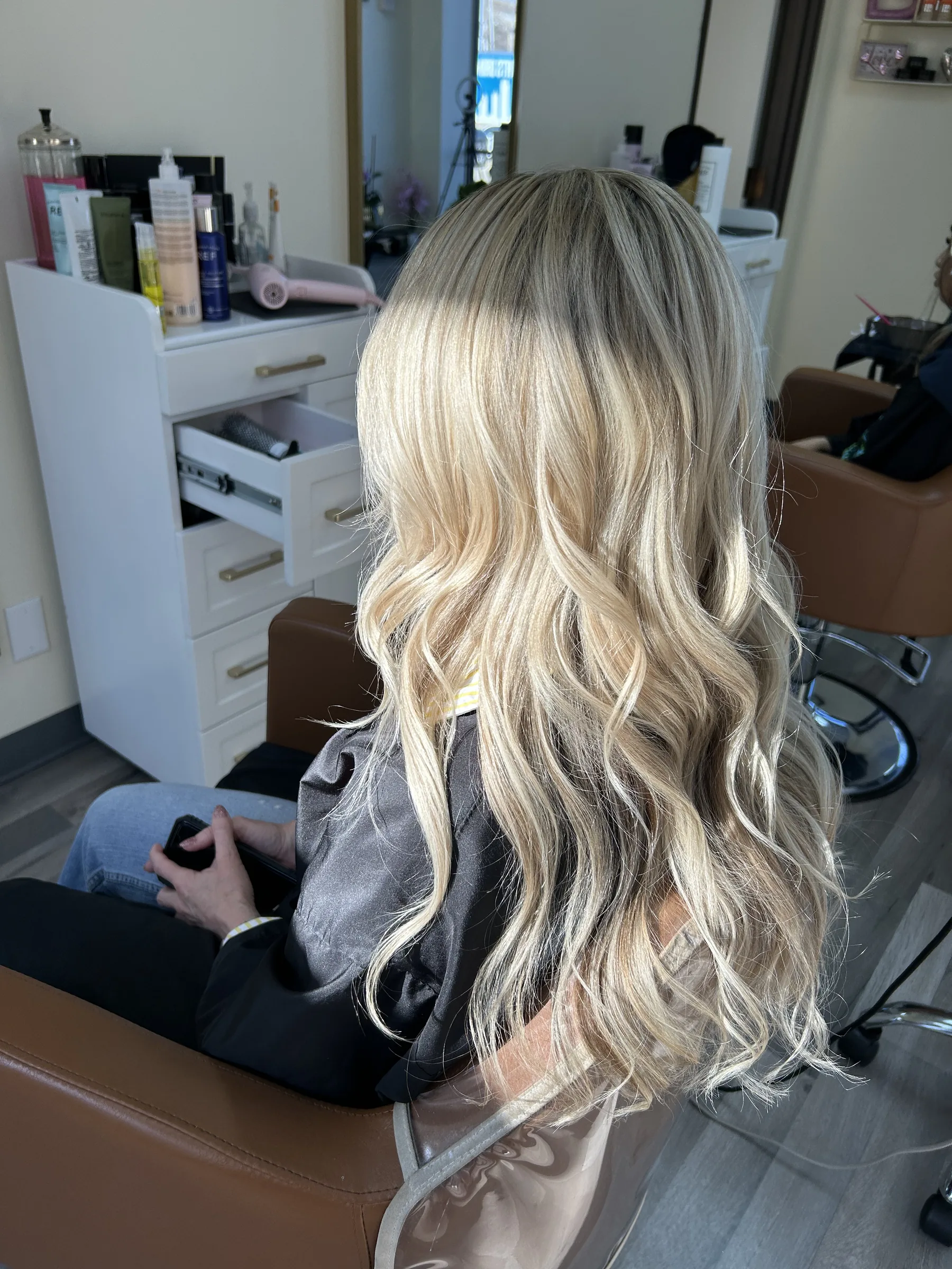 Blonde woman with long wavy hair sitting in a salon chair from behind.