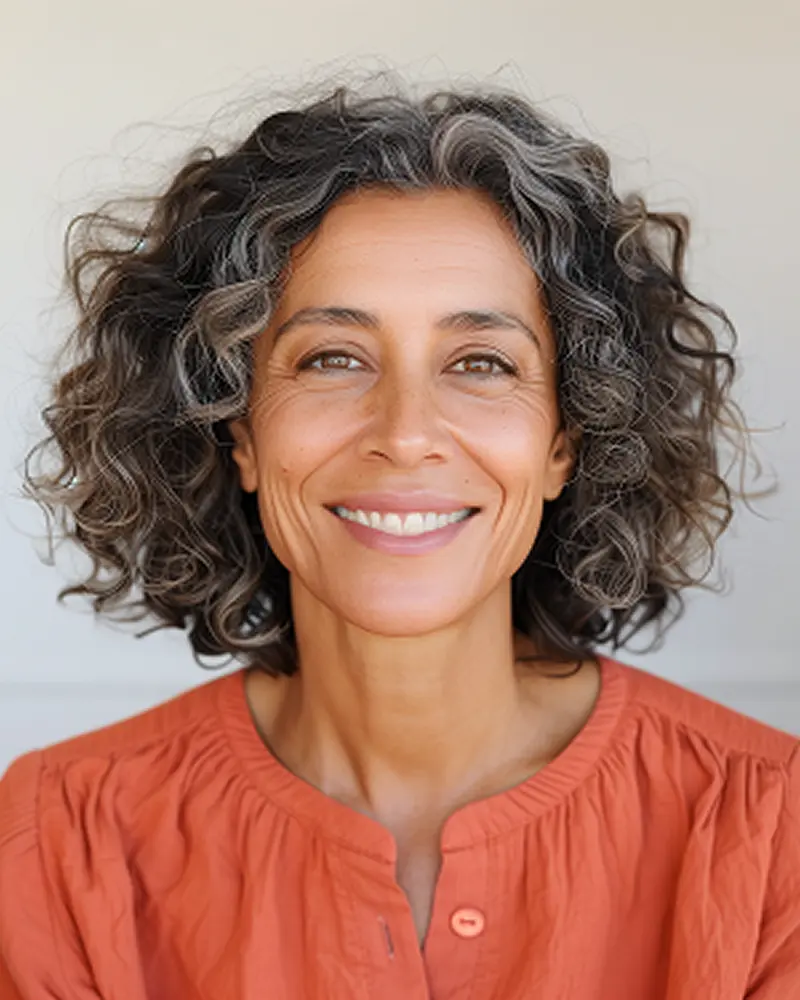 Smiling middle-aged woman with curly salt-and-pepper hair wearing an orange blouse.