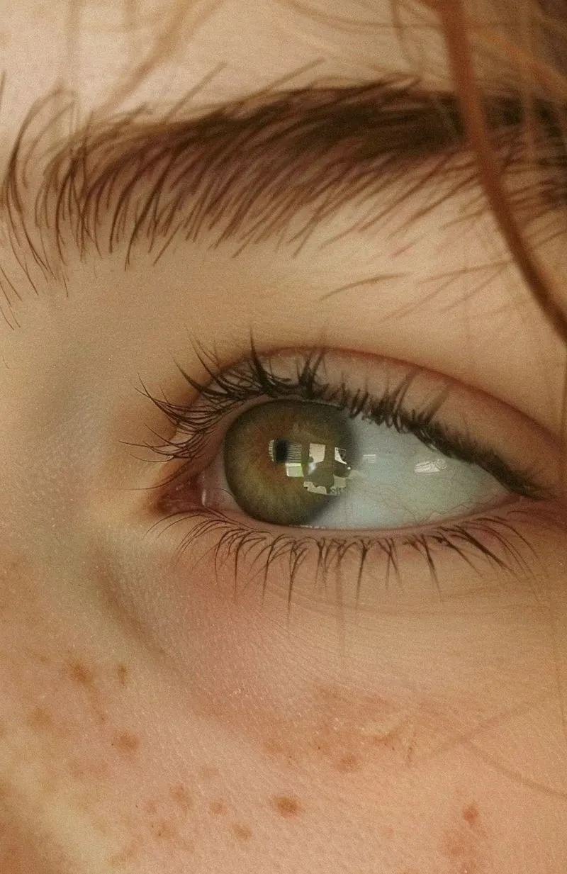 Close-up of a green eye with long eyelashes and light freckles on the skin.