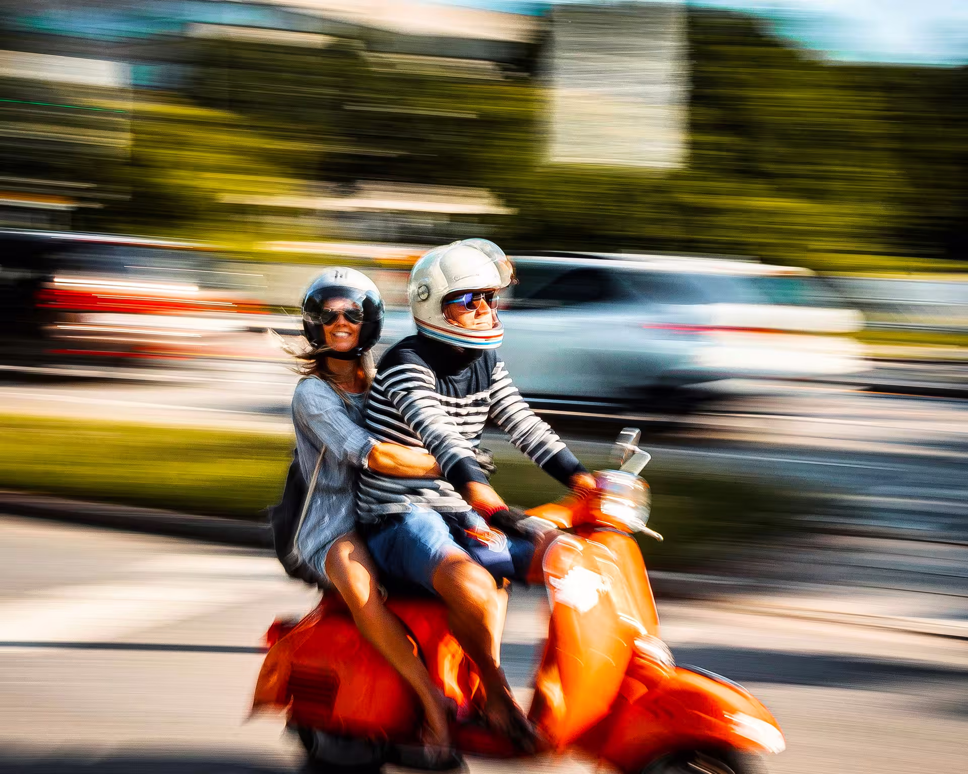 Two people wearing helmets riding a red scooter on a blurred urban street.