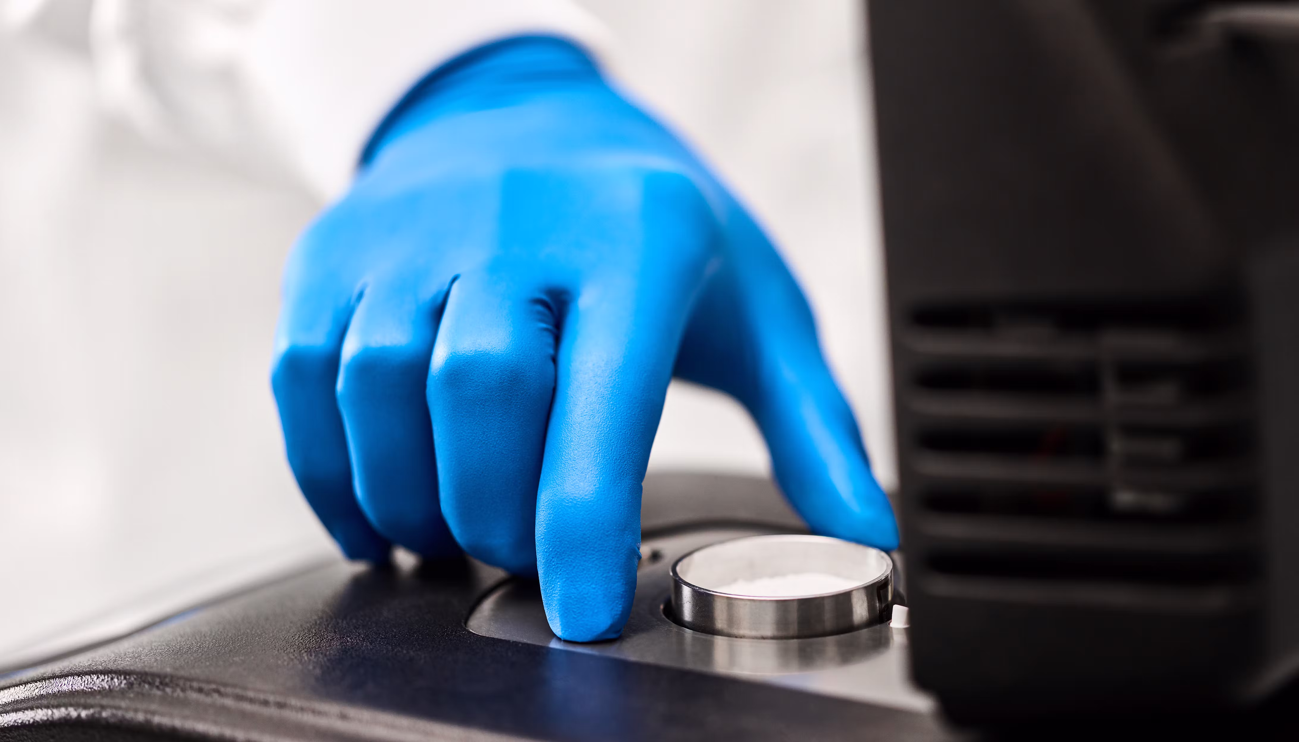 Blue-gloved lab technician placing a small metal sample cup into an AQUALAB water activity meter for precise moisture analysis