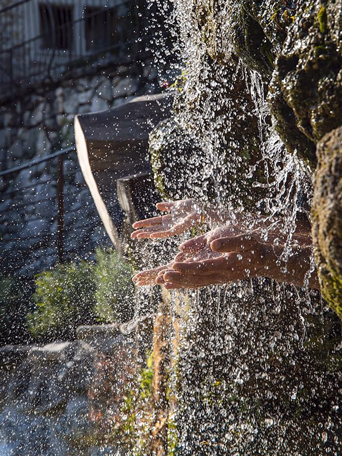 Deux mains s'ouvrent pour traverser l'eau claire d'une cascade. Les gouttes d'eau pure rebondissent sur la roche couverte de mousse. Cette eau naturelle apporte une belle fraîcheur au milieu de l'été — un contact sensoriel direct avec la nature absolue.