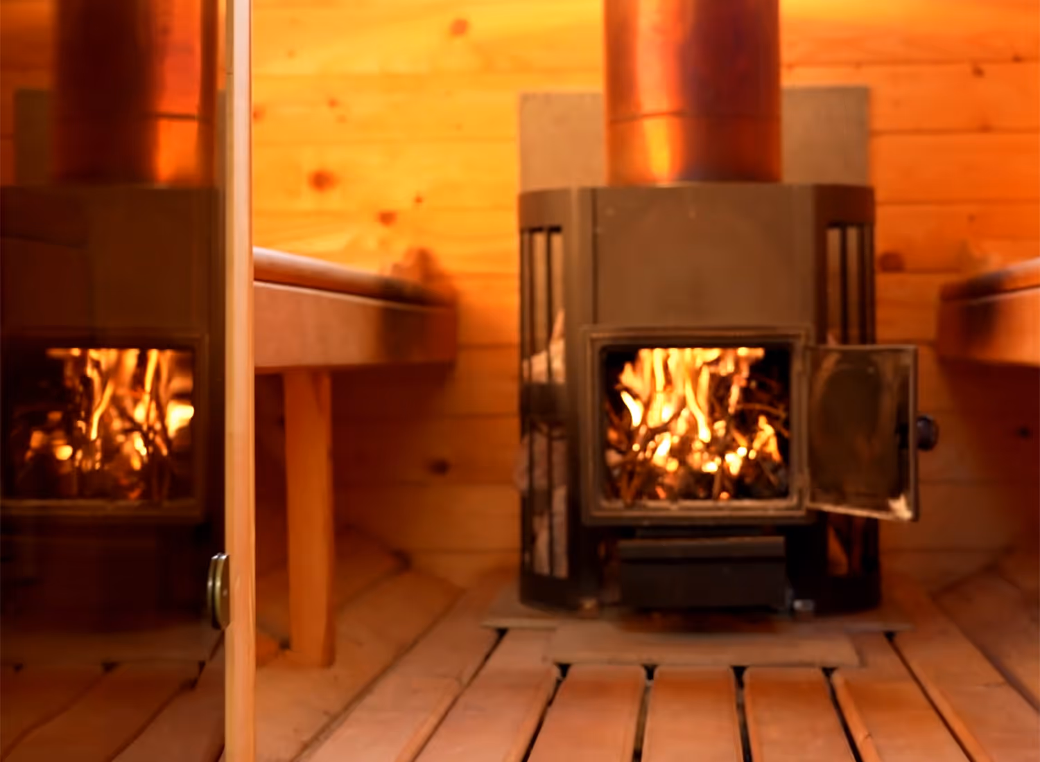 ntérieur du sauna privatif en bois avec ses banquettes et la chaleur de son poêle à bois traditionnel en plein fonctionnement.