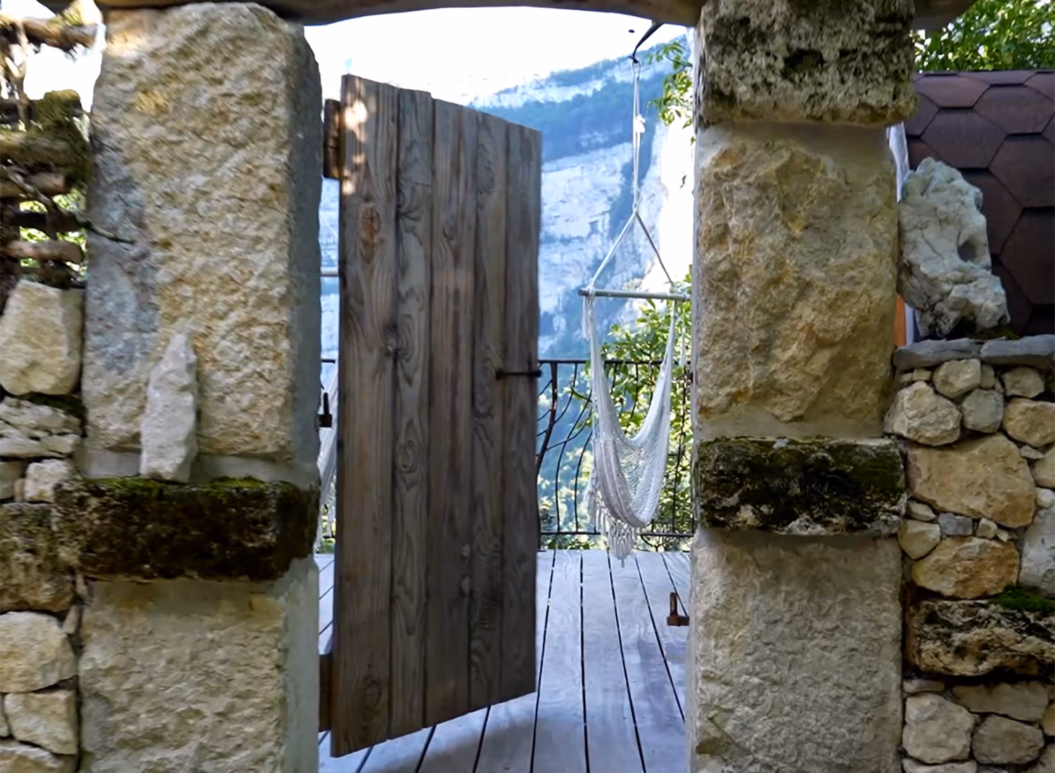 Entrée de l'espace détente extérieur par une arche en pierre et une porte en bois massif, ouvrant sur la terrasse suspendue et les montagnes.