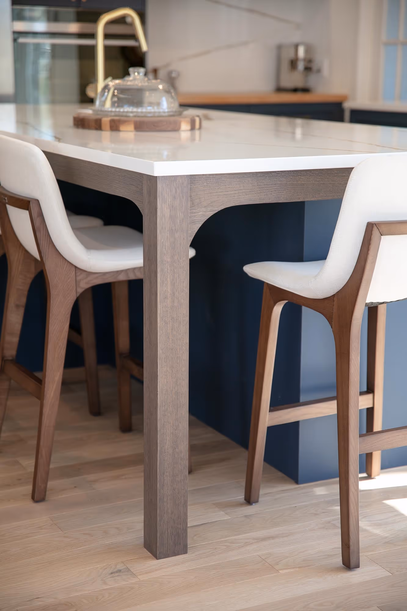 Chaises modernes en bois avec assises blanches autour d'un comptoir de cuisine avec plan de travail blanc et robinet doré.