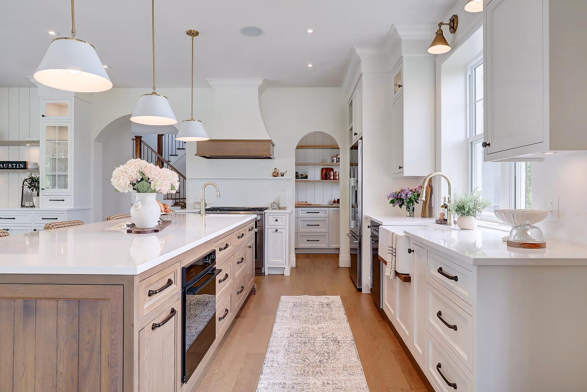 Cuisine moderne lumineuse avec îlot central en bois clair, comptoirs blancs, lampes suspendues, et décor floral.