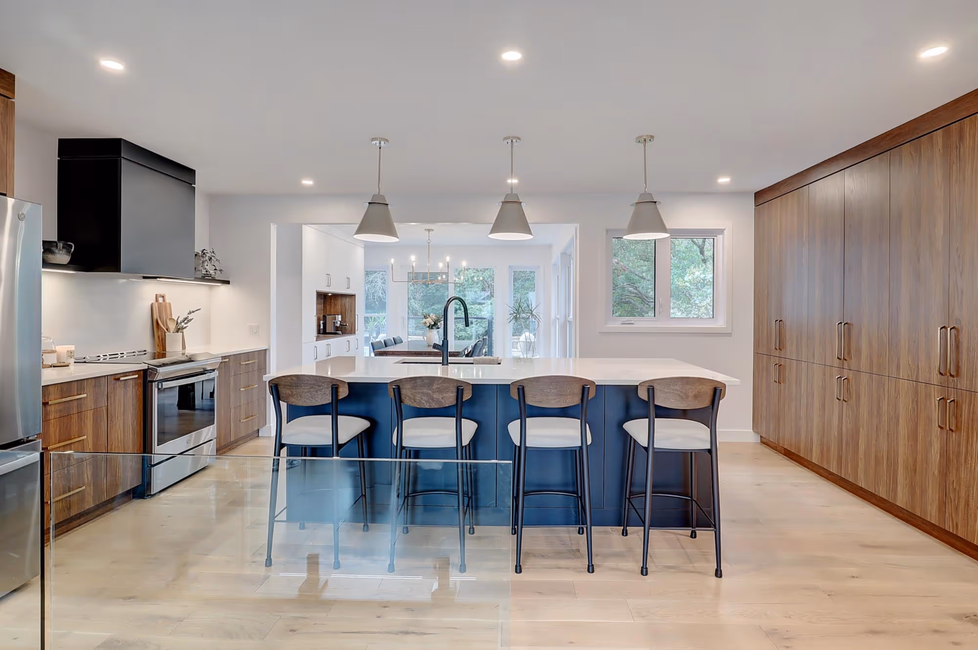 Cuisine moderne avec un îlot central bleu foncé, quatre tabourets hauts, des armoires en bois et des appareils électroménagers en acier inoxydable.