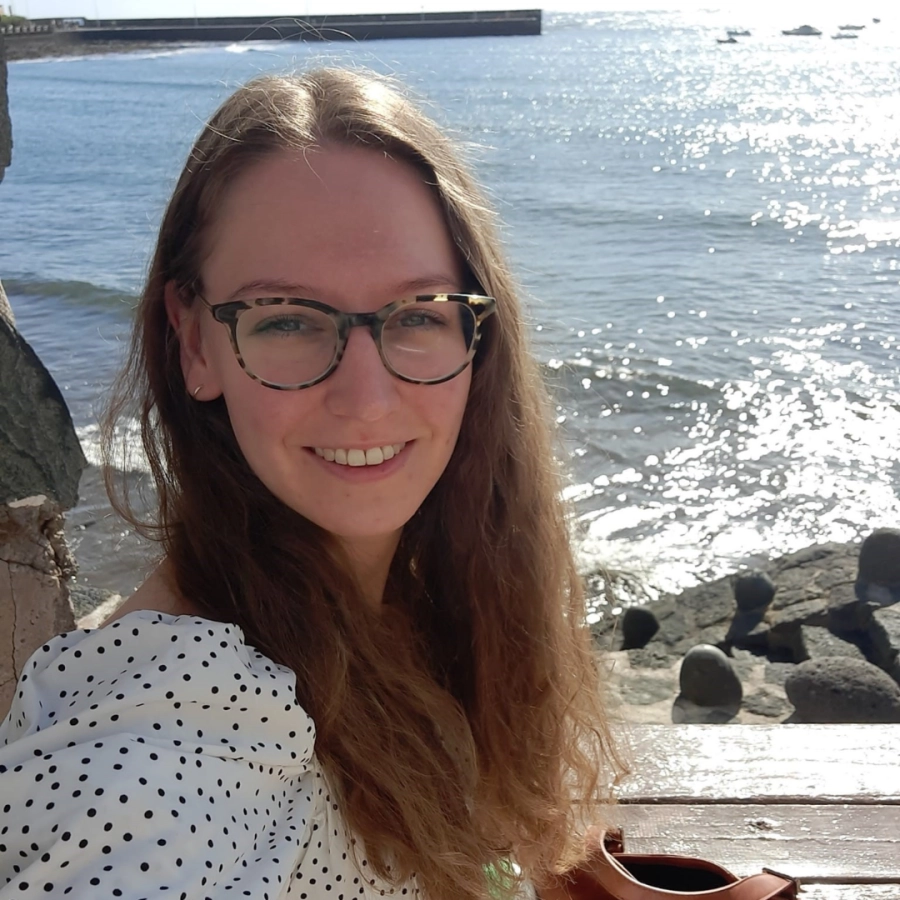 Portret van een vrouw met een bril die glimlacht naar de camera aan zee op een zonnige dag.