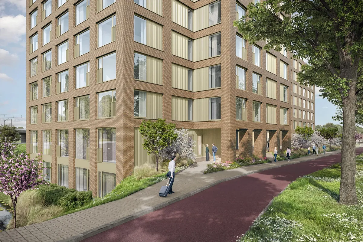 Hoekaanzicht van een modern bakstenen woongebouw met grote ramen, groen aangelegde buitenruimte en mensen die lopen langs een rood fietspad.