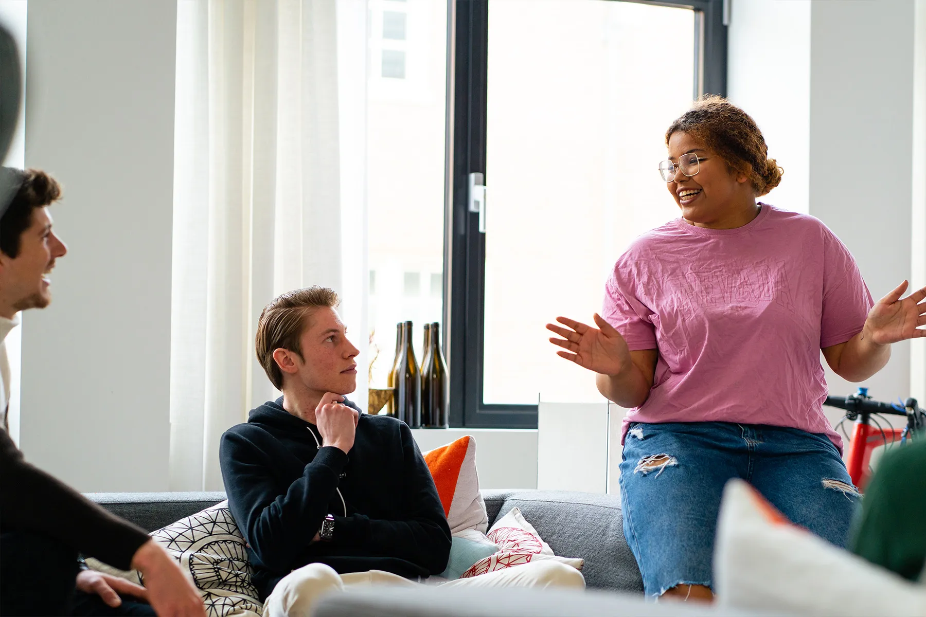 Groep jonge mensen die zitten en staan in een woonkamer en samen in gesprek zijn binnenshuis.