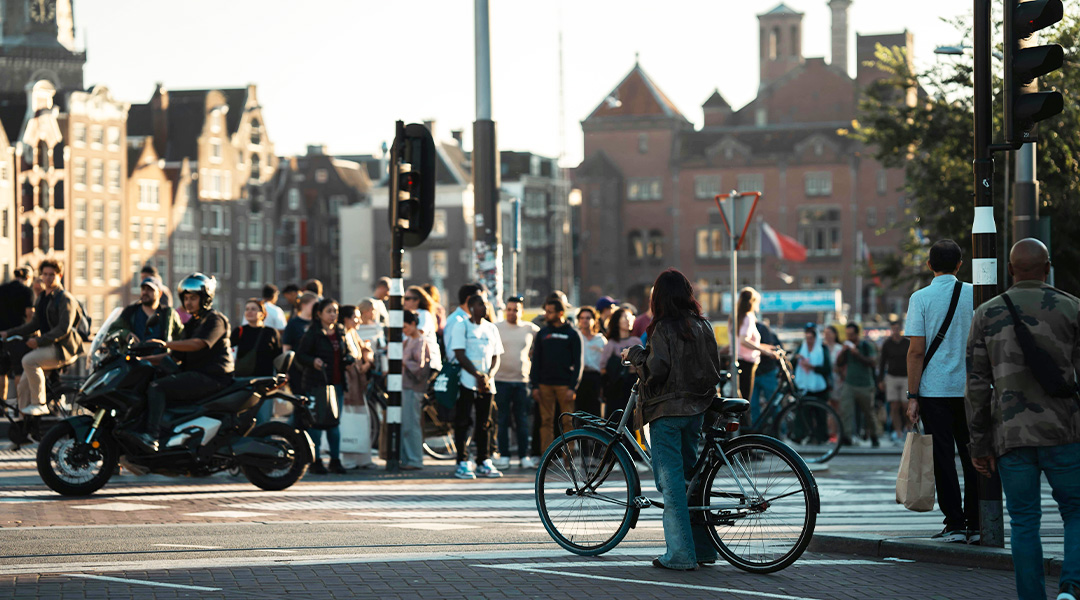 Mensen die wachten bij een druk stadskruispunt, met fietsers en voetgangers verzameld bij een oversteekplaats in een stedelijke omgeving.