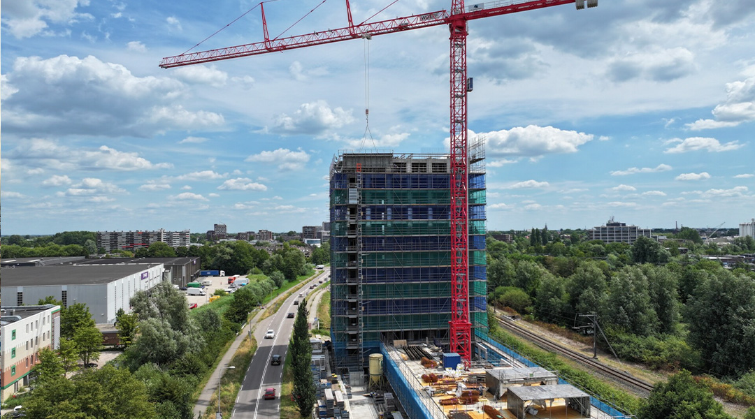 Colivinggebouw in aanbouw in Gouda, met steigers en een kraan zichtbaar in het omliggende stedelijke landschap.