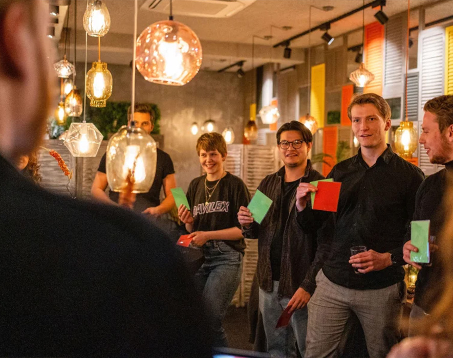 Leden van het woonpanel komen binnen samen en houden gekleurde kaarten omhoog terwijl zij stemmen over ideeën tijdens een communitybijeenkomst in een gedeelde colivingruimte.