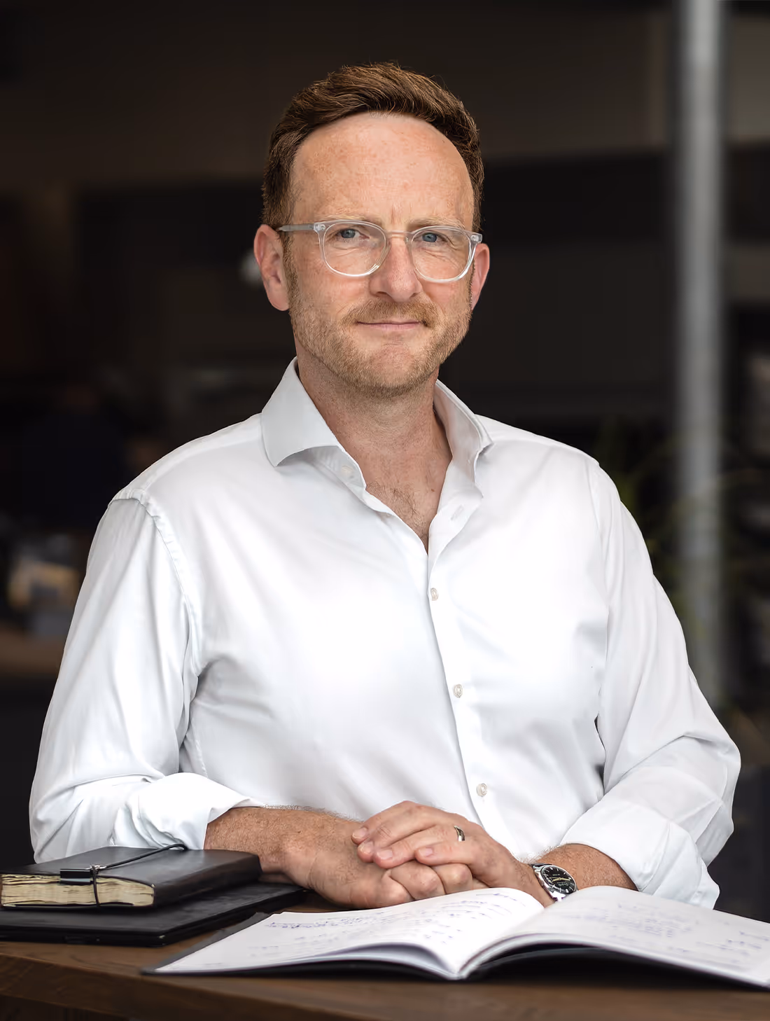 Ralph Steffens sitzt an einem Tisch mit geöffnetem Buch und Notizbüchern.