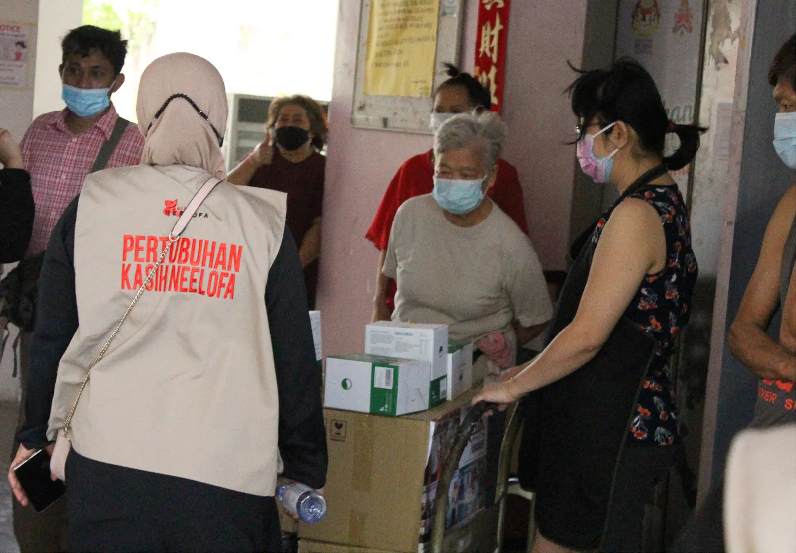 Masked volunteers and elderly people distributing boxed supplies indoors.