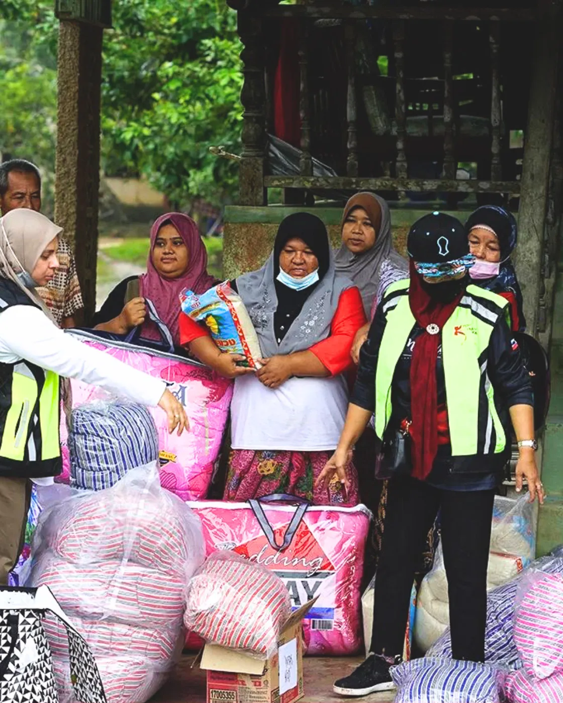 Group of women, some wearing headscarves, organizing and distributing large bags of supplies and food aid outdoors.