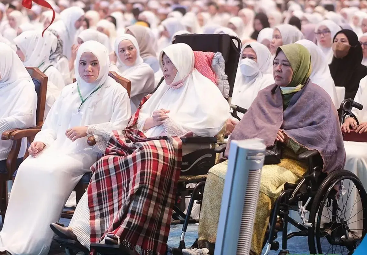 A group of Muslim women, some seated in wheelchairs and others wearing white hijabs, attending a formal event.