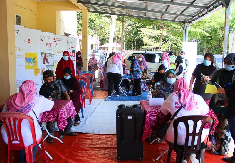 A busy community health screening setup with people wearing masks sitting and waiting under a covered outdoor area.
