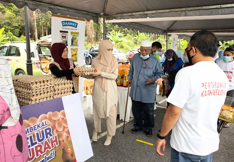 Women distributing trays of eggs to elderly and masked people at an outdoor community food aid event.