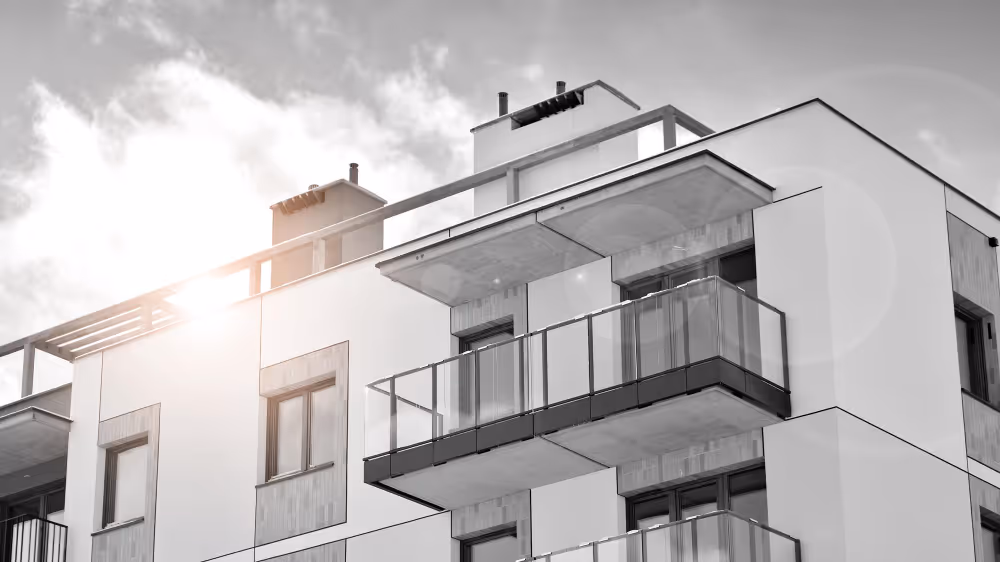 Moderner Wohnhaus mit Balkonen und Sonneneinstrahlung am bewölkten Himmel.