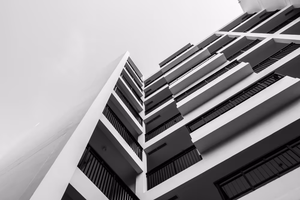 Schwarz-weißes Foto eines mehrstöckigen Gebäudes mit Balkonen, fotografiert aus der Froschperspektive nach oben.