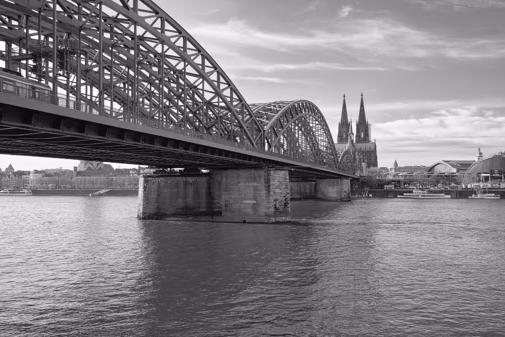 Die Hohenzollernbrücke überspannt den Rhein mit dem Kölner Dom im Hintergrund bei klarem Himmel.