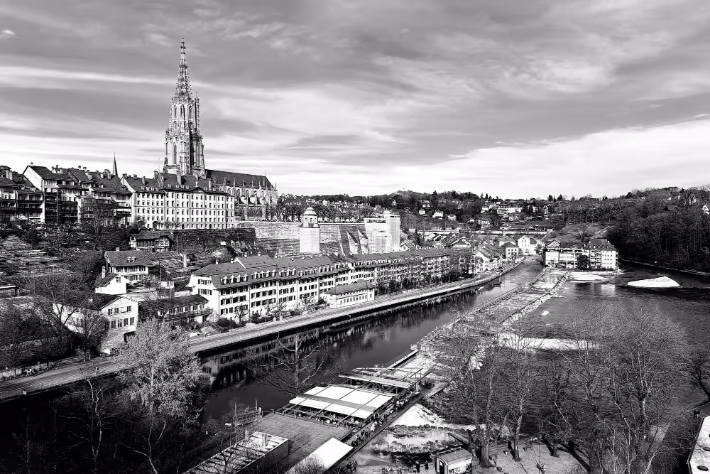 Panoramablick auf Bern mit Fluss Aare, historischen Gebäuden und dem markanten Turm des Berner Münsters.