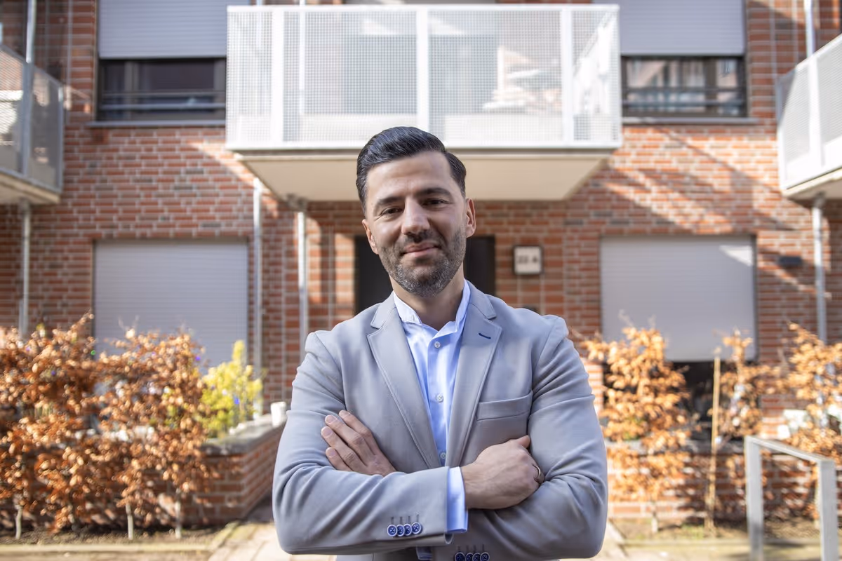 Gökhan Gül, Immobilienmakler in Bremen, mit verschränkten Armen vor einem modernen Backsteinhaus