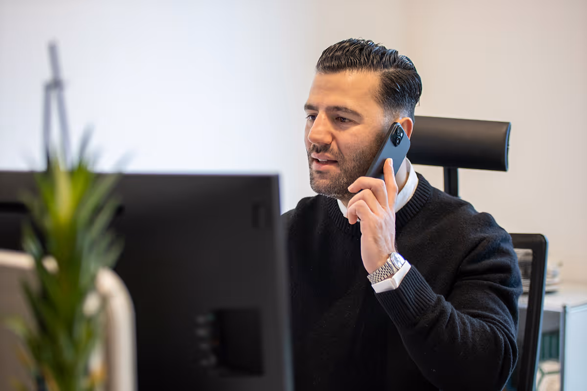 Mann spricht am Telefon und sitzt vor einem Computerbildschirm in einem Büro.