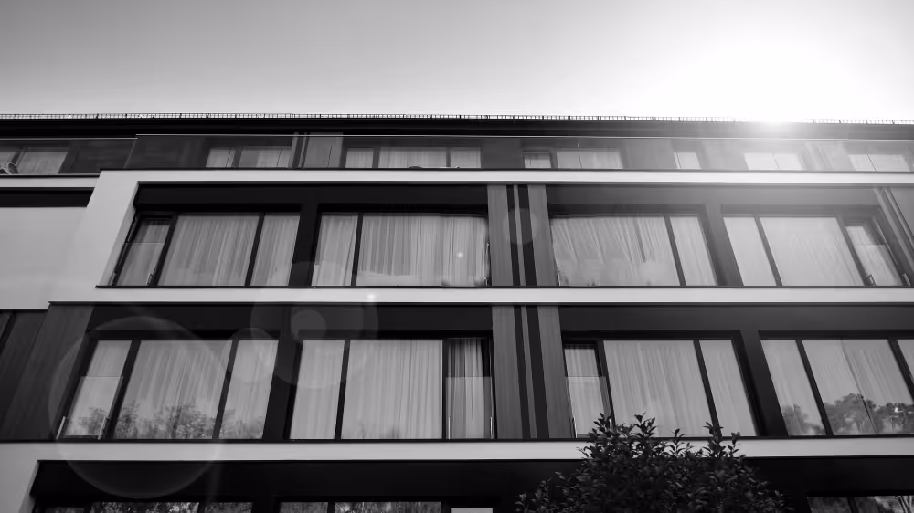 Moderne Gebäudefassade mit großen Fenstern und Sonneneinstrahlung von oben rechts.