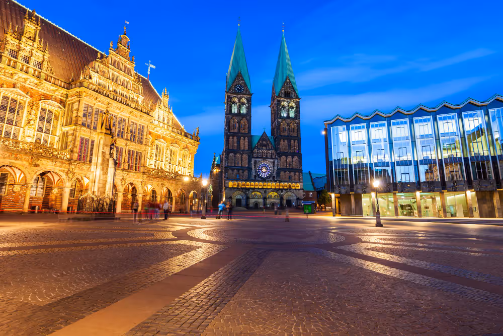 Beleuchteter Marktplatz bei Dämmerung mit historischem Rathaus und Dom mit zwei Türmen in Bremen.