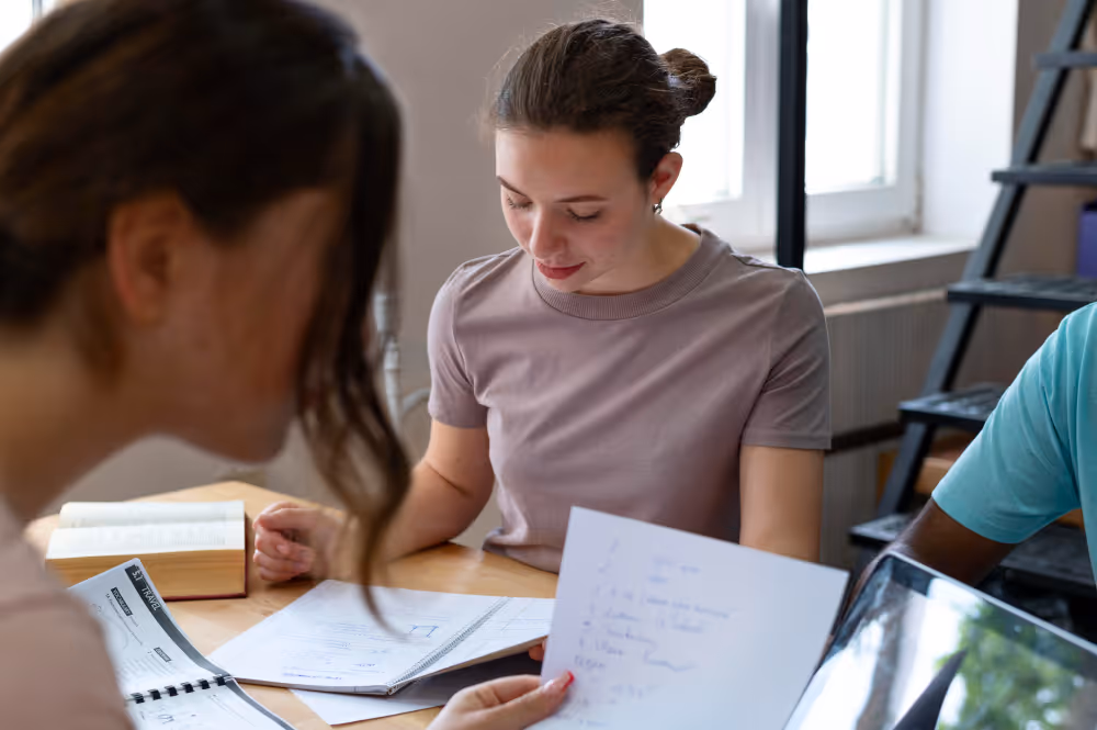 Junge Menschen arbeiten zusammen an Dokumenten und Notizen an einem Tisch in einem hellen Raum.