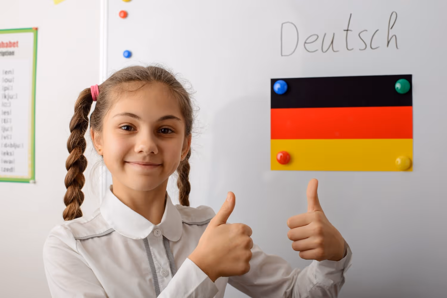 Mädchen mit Zöpfen vor einer Tafel mit der deutschen Flagge und dem Wort Deutsch zeigt zwei Daumen nach oben.